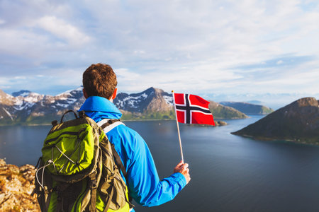 travel to Norway, hiker traveler with backpack holding norwegian flag and looking at beautiful fjord landscapeの写真素材