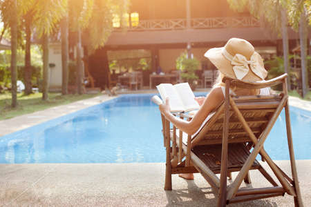 relaxation concept, woman reading book near swimming pool of hotelの写真素材