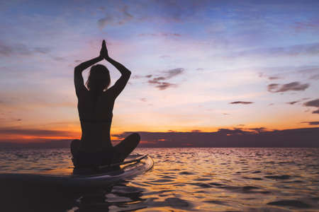 yoga on sup board, silhouette of woman on the beachの写真素材