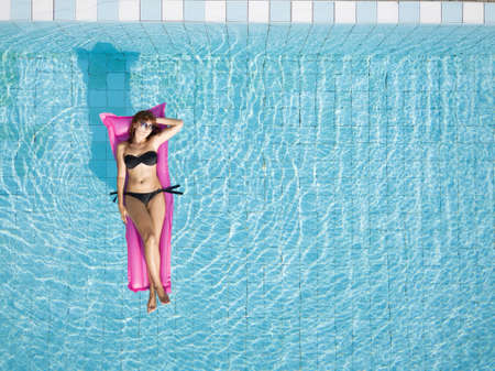 woman in bikini relaxing on inflatable mattress in the swimming pool of hotel, beach vacation, holidays background with copy spaceの写真素材