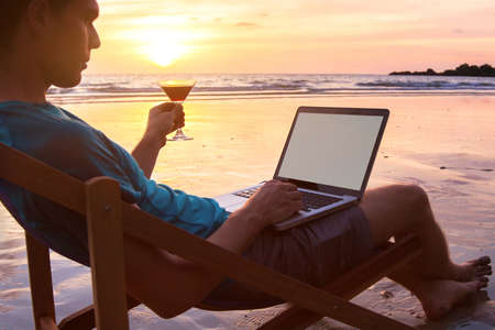 successful businessman freelancer working on computer at sunset beach, laptop with empty screen and copyspaceの写真素材