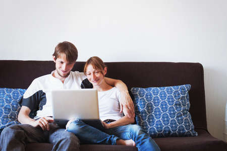 young couple looking at computer and smiling, family sitting on the couch at homeの写真素材