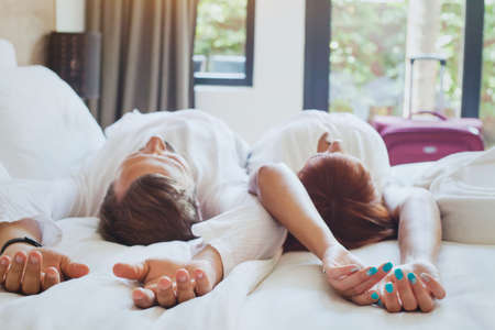 hotel guests relaxing on the bed in their room, couple traveling to luxurious resortの写真素材