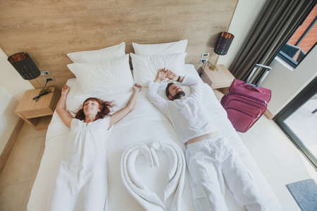 happy couple in luxury hotel room, holidays travel accommodation, top view of smiling man and woman lying down on the bedの写真素材