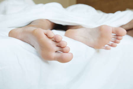 sweet sleep on comfortable mattress, feet of person in the bed under white blanketの写真素材