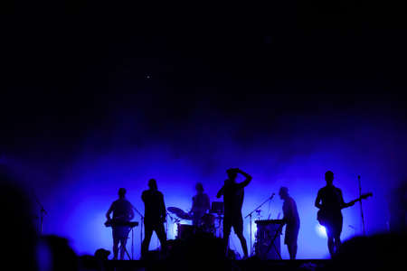 music band playing on concert stage, silhouettes of musicians unrecognizable, group of people singing together in rock festivalの写真素材