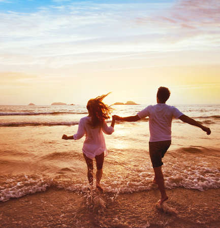happy couple on honeymoon vacation travel, romantic dream beach holidays, happiness background, silhouettes of man and woman running to the sea at sunset togetherの写真素材