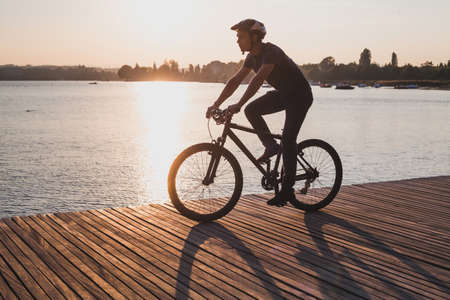 silhouette of man on bicycle in sunset city near lake, sport cycling active leisureの写真素材