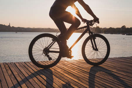 man riding bicycle at sunset, cycling in summer, silhouette of cyclist near the lakeの写真素材