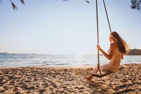 dream and happiness concept, romantic beautiful carefree woman relaxing on the swing at sunset beach, summer holidays, vacation travel and relaxation, inspiring landscapeの写真素材