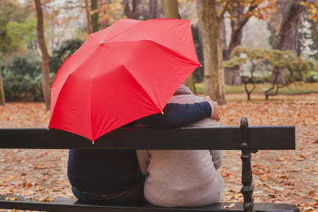 comforting and psychological support, care concept, man hugs woman under umbrella in autumn parkの写真素材