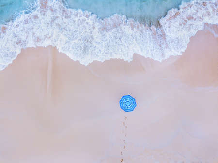 Travel to beautiful beach, holidays, vacation getaway on paradise island, aerial top down view of ocean wave and person with blue umbrella.の写真素材