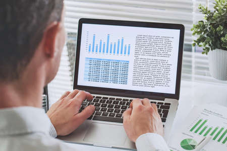 business man reading financial analytics report with charts on screen of laptop computer, investment conceptの写真素材
