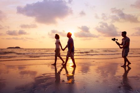 filmmaker filming video of couple with camera stabilizer on the beach at sunset, professional...
