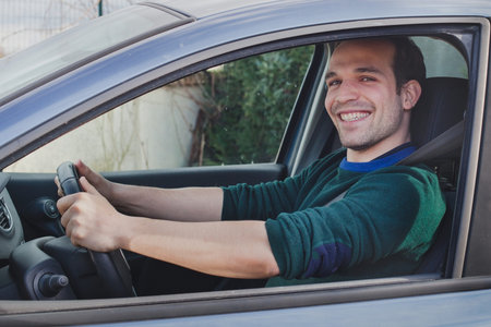 happy proud young man driving car, smiling and looking to camera