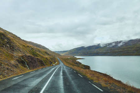 travel background, beautiful asphalt road in fjords in Iceland, cloudy landscape, roadtrip in autumnの写真素材