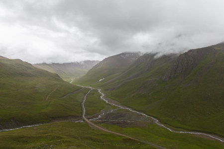 road in Enilchek valley with green mountains and cloudy sky in Kyrgyzstanの写真素材