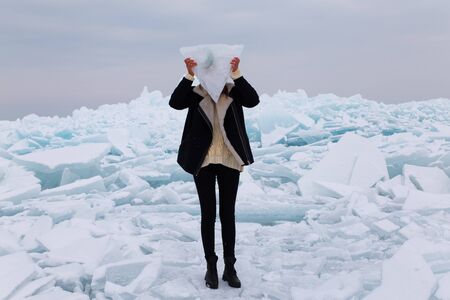 girl covering her face with triangle block of ice staying on hummock in frozen lake Kapchagai near Almaty, Kazakhstanの写真素材
