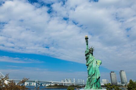 TOKYO, JAPAN - NOVEMBER 11, 2018: liberty statye in Odaiba island with blue sky, buildings, raninbaw bridge and clouds in backgroundのeditorial素材