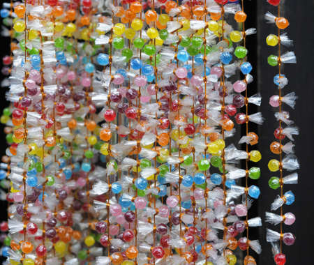 Sugar candy beads in transparent film tied together with golden cord; the strings hung for display; backgroundの写真素材