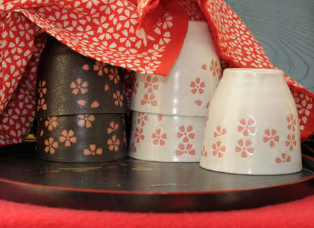 Japanese porcelane cups under red cotton cloth with matching floral design. The cups are beautifully glazed. The shot was made in one of the small stalls offering tea by Kiomizu Dera temple in Kyoto, famous for its tasty water.の写真素材