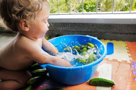 One year old baby boy splashing in a bown of water with cucumbersの写真素材