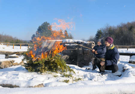 Mother and a three year old baby boy by a camping fire in a winter forest on a sunny dayの写真素材