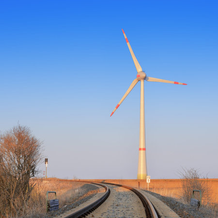 Railroad leading towards modern windmill on a sunsetの写真素材