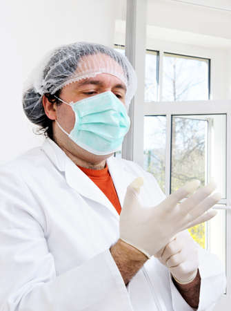 Doctor in white gown and protective mask puts on disposable glovesの写真素材