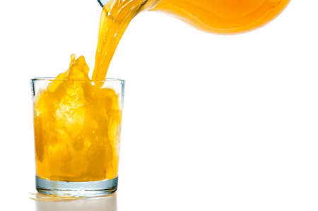 Orange juice pouring from the jar into a glass on a white backgroundの写真素材
