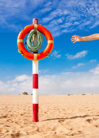 Hand reaches for Life Buoy attached to a wooden pole; bright daylight on a beach, copyspaceの写真素材