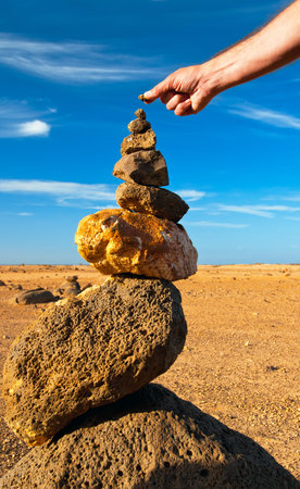 Man puts a tiny stone to complete stone pyramid in the desertの写真素材