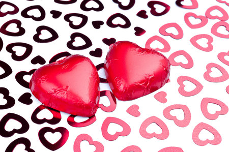 Two chocolate hearts in aluminium foil on shiny pink heart