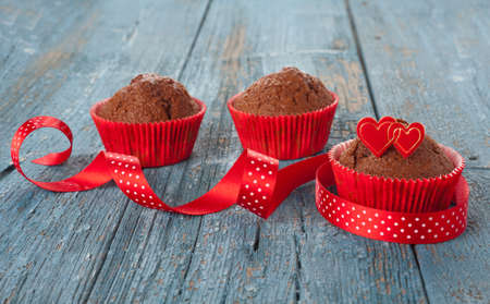 Chocolate muffins decorated with hearts cake top and a ribbon on old wooden tableの写真素材