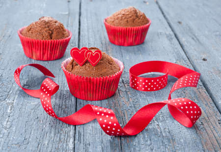 Chocolate muffins in red paper cups decorated with hearts and a ribbonの写真素材