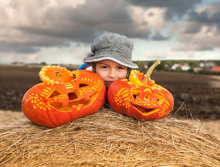 Little boy with two carved halloween pumpkins on a roll of hayの写真素材