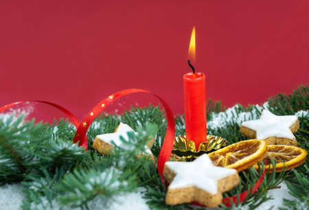 Xmas tree with snow, cookies, dry oranges and a burning candle on dark red backgroundの写真素材
