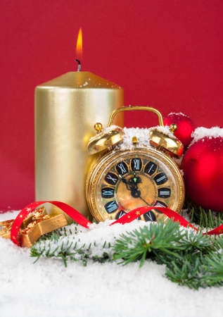 New Year decorations  an old clock showing five to twelve, burning candle and winter decorations on red background, spaceの写真素材