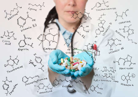 Healthcare worker wit hands full of pills surrounded by formula of antibiotica, vitamines and food additivesの写真素材