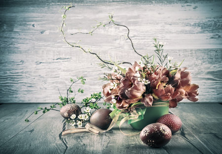 Orange fluffy tulips and ornate Easter Eggs on wooden table, tinted image, text space