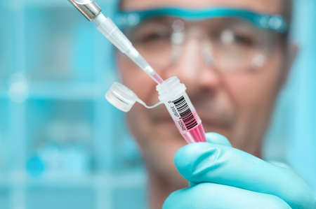 Scientist or tech holds liquid biological sample in gloved handsの写真素材