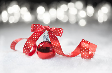 Red bauble with matching ribbon with polka dots on snowの写真素材