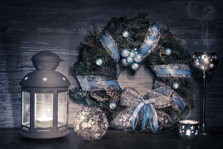Decorative lantern, candles and Christmas wreath with decoratons on woodの写真素材