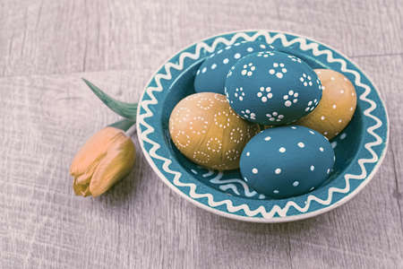 Blue and orange Easter eggs on wood and a tulip. Toned imageの写真素材