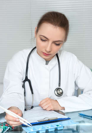 Physician or nurse in white coat selects pills for a patient checking his recordsの写真素材