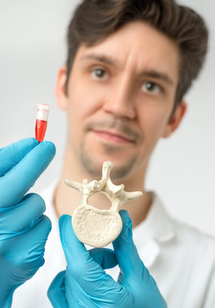 Doctor or scientist holds vertebra and a tube with red liquid in gloved hands. Shallow DOF, focus on the objects.の写真素材