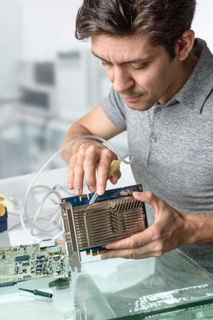 Young male tech cleans faulty computer processor in hardware repair workshop. Focus on the face and fingersの写真素材