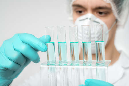 Keen scientist in protective wear performs protein assay. Shallow DOF, focus on the tubes and gloved hand.の写真素材