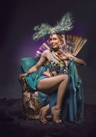 European female dancer in exotic costume sits in armchair on dark backgroundの写真素材