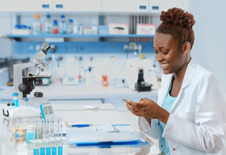 African-american biologist in the lab texting someone on her mobile with a smileの写真素材